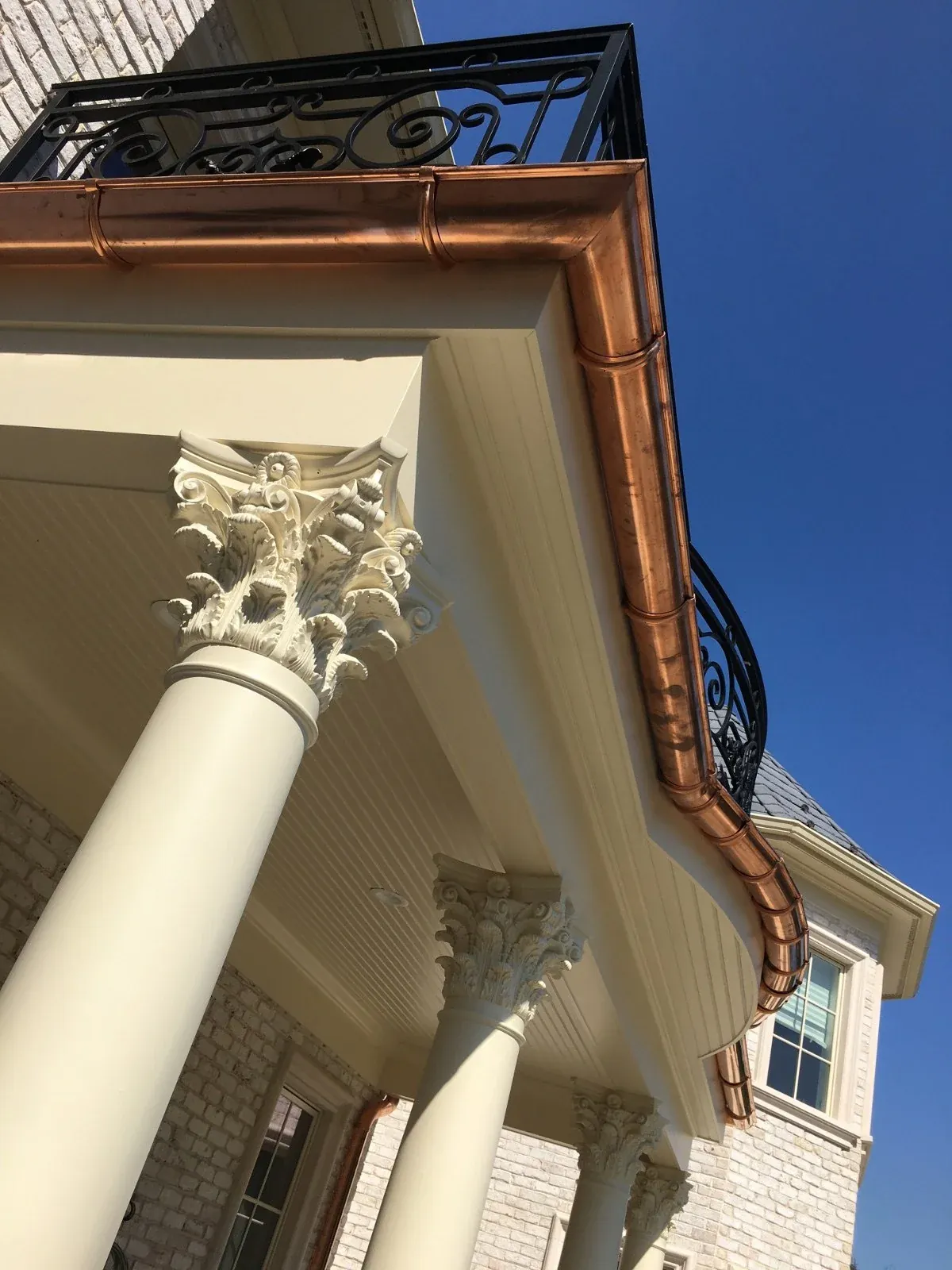 Copper gutter running along the roof edge above white columns on a brick house