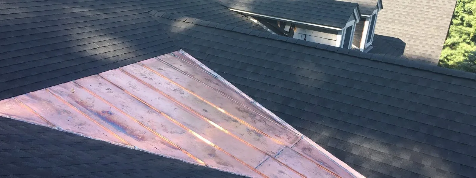 Copper valley set into a dark shingle roof beside a dormer