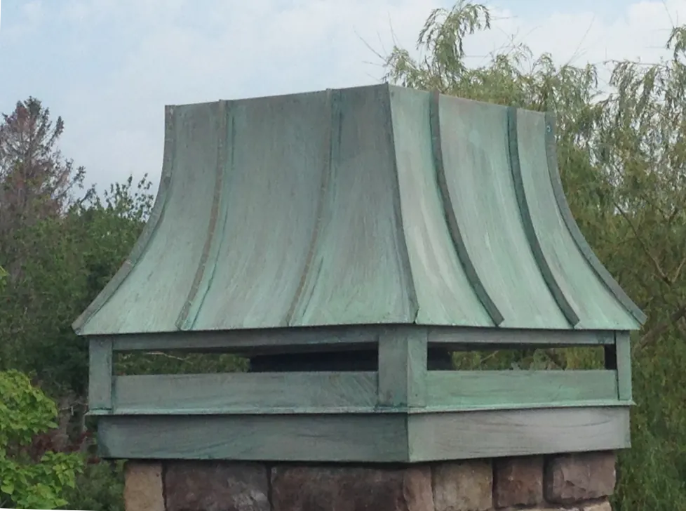 Aged copper cupola with a green patina on a stone chimney base