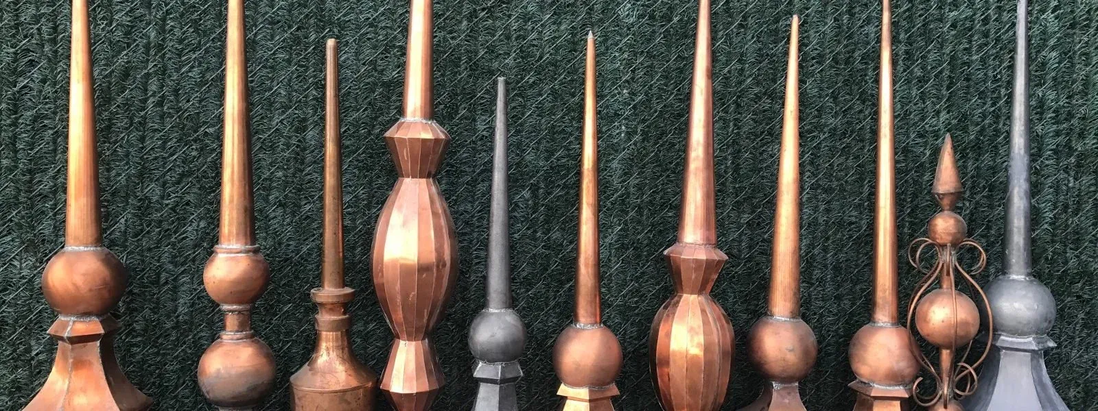 A row of copper finials in different shapes and sizes, from slim spires to ball-and-spire styles