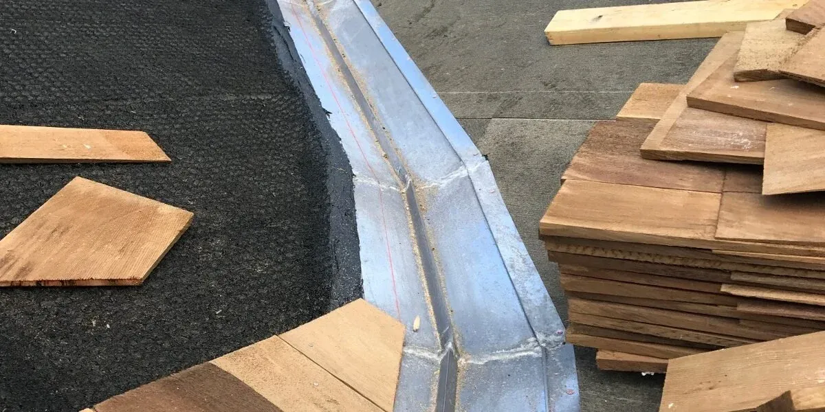 Metal valley gutter on a roof deck with cedar shingles stacked beside it