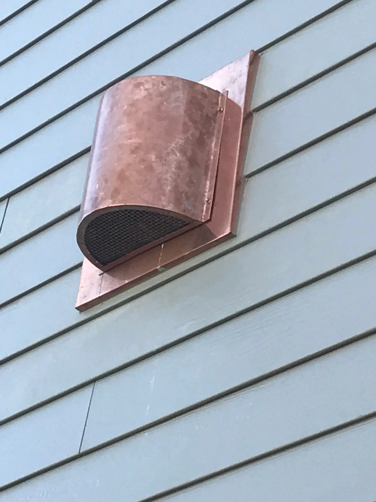 Copper vent hood with a mesh screen mounted on lap siding
