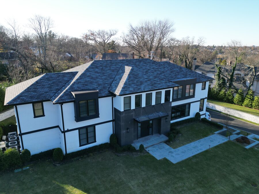 Aerial view of a two-story white house with a dark slate-look roof, black-framed windows and a stone walkway