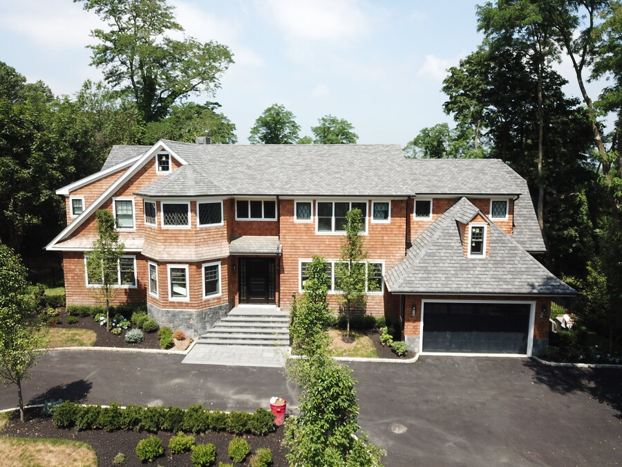 Cedar-shingle house with a gray shingle roof, a black garage door and a dark asphalt driveway