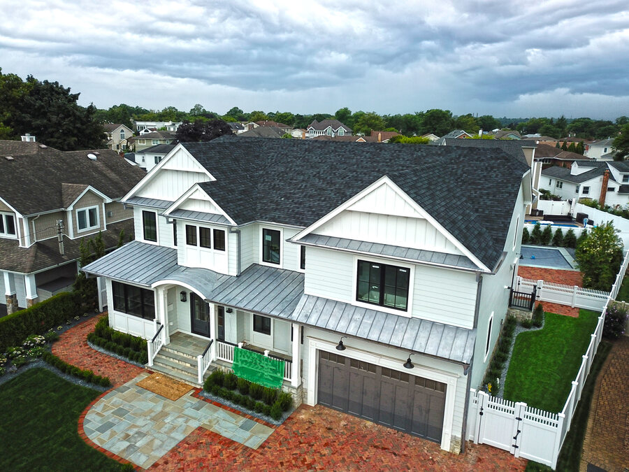 White board-and-batten house with a dark shingle roof, gray metal roofing over the porch and garage, and a white fence