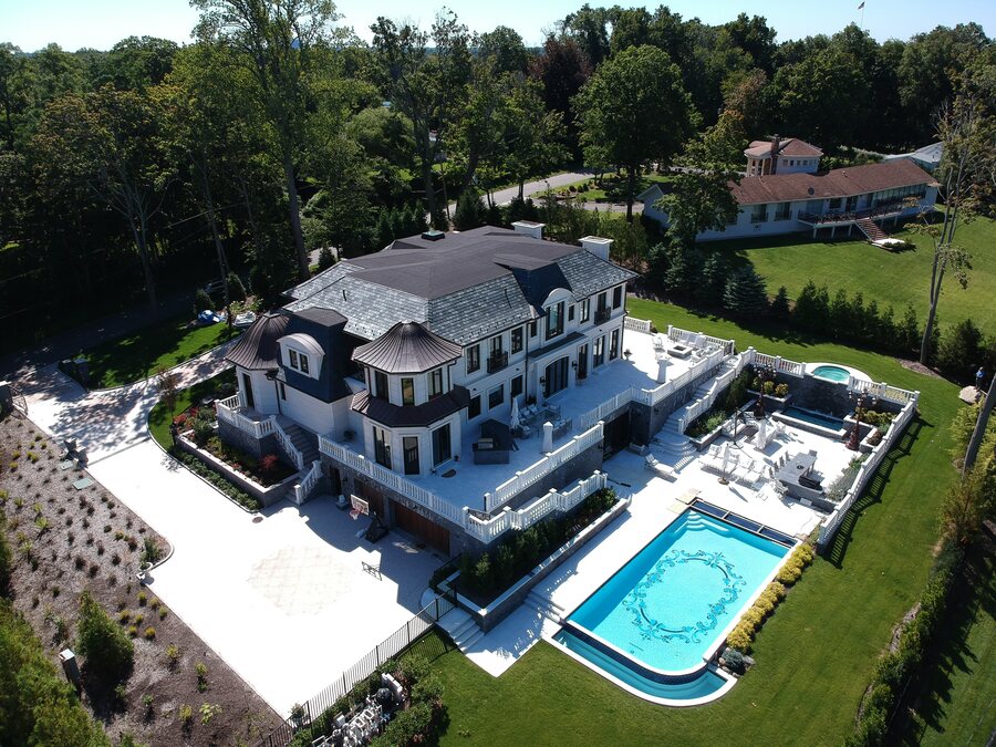 Aerial view of a large estate with a dark hipped roof, copper-look turret roofs, white balustrades and a blue pool