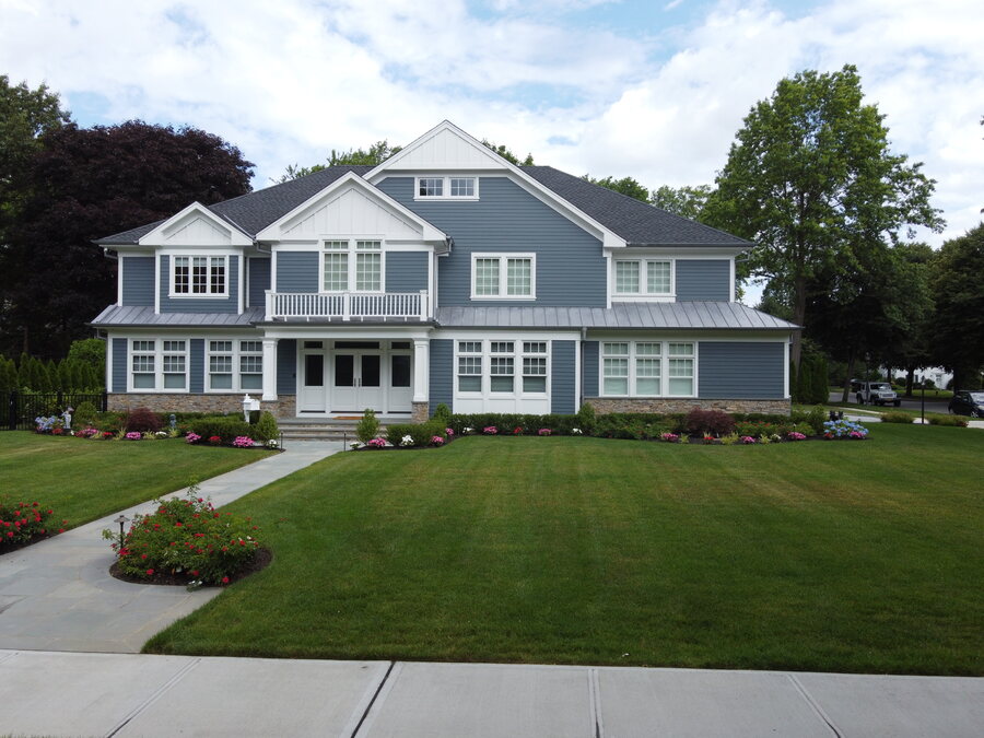 Blue-gray siding house with white trim, a metal-roofed front portico, stone base and a striped green lawn