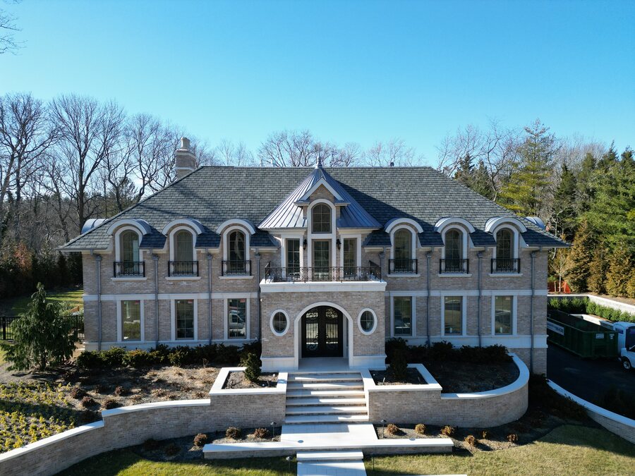 Front view of a symmetrical brick house with arched dormers, a slate-look roof, a balcony and a curved stone stair wall