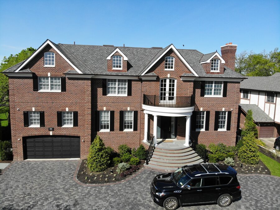 Red brick house with black shutters, a curved front balcony, a garage and a black SUV parked on a paver driveway