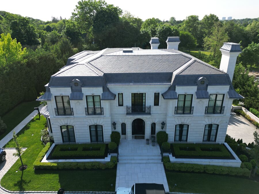 Cream limestone-colored house with a slate-look roof, metal-clad dormers and a clipped boxwood garden