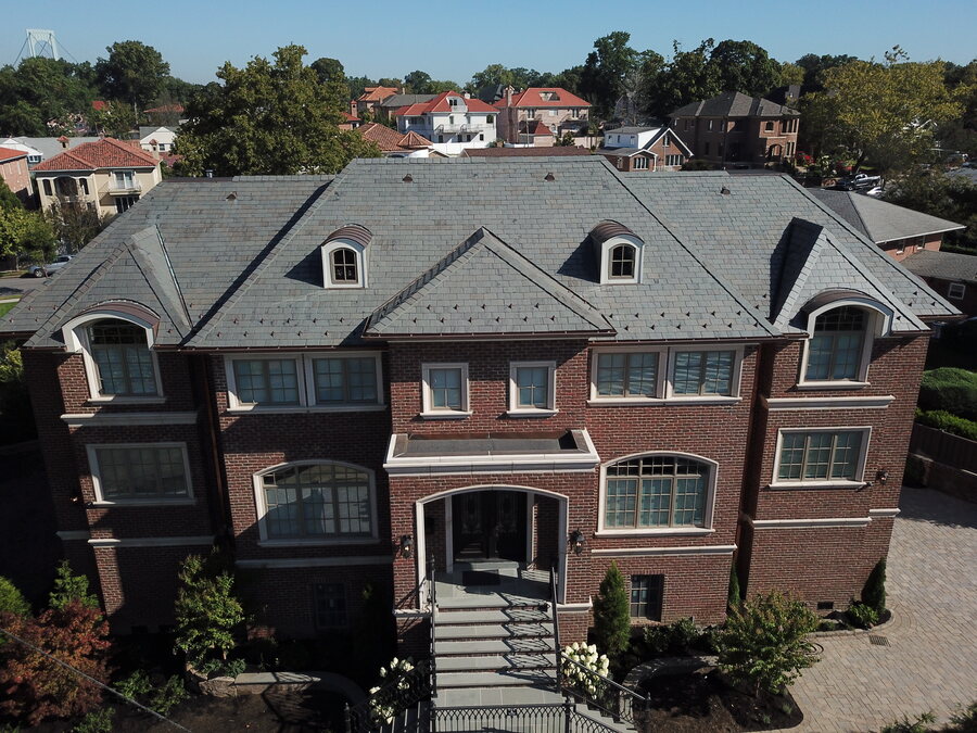 Red brick house with a dark slate-look roof, arched dormers and a paver driveway