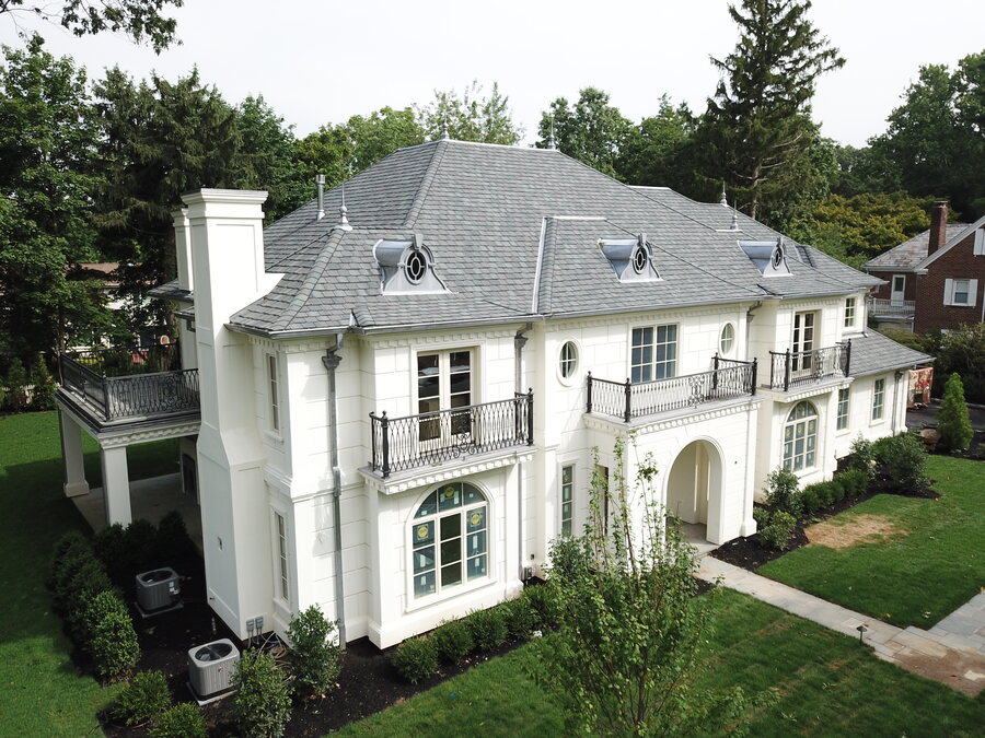 Cream stucco house with a gray slate-look roof, a stone chimney and iron balconies