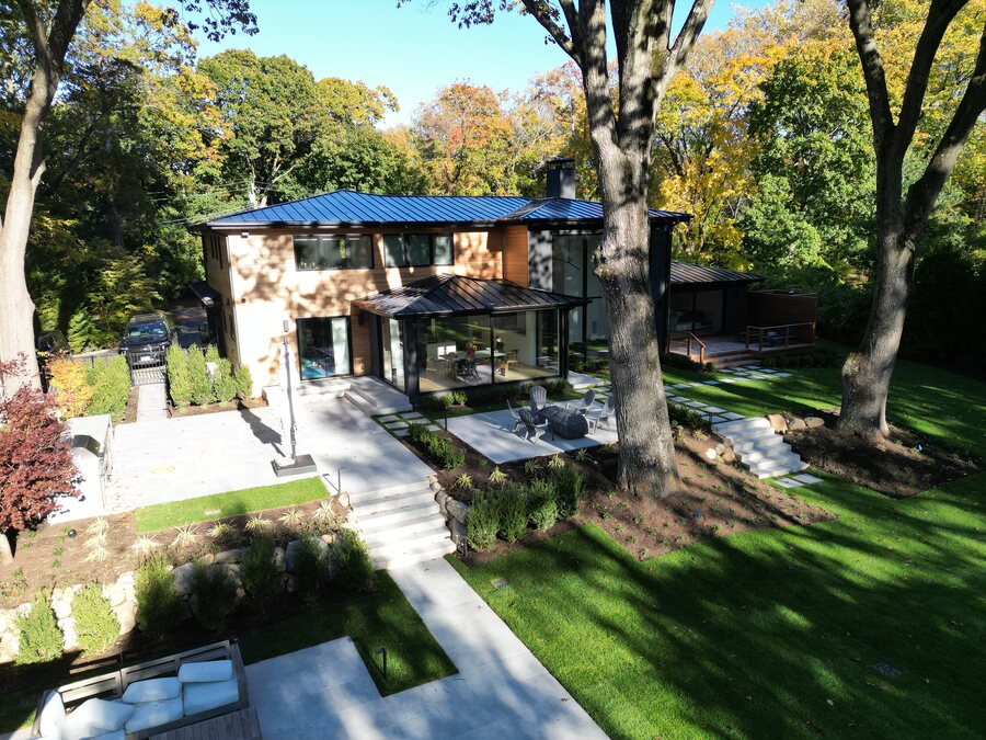 Modern two-story house with a blue standing-seam metal roof and large glass walls among tall trees