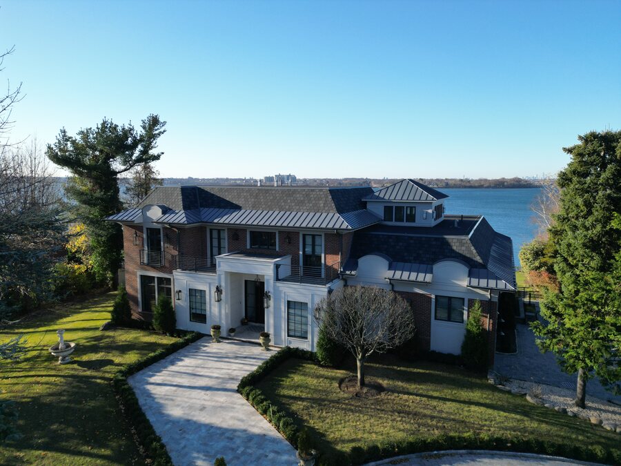 Waterfront house with a dark standing-seam metal roof, stone and brick walls and a paver walkway