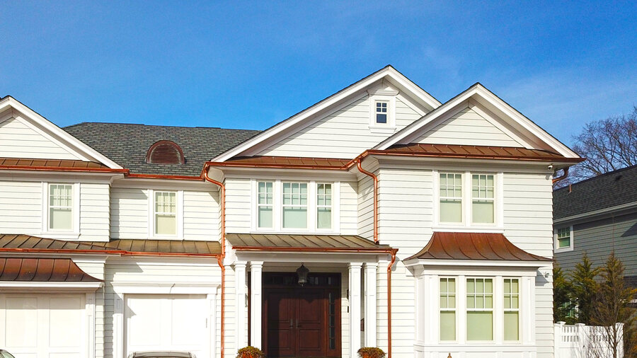 White house with copper standing-seam awnings and copper gutters over the garage and entry