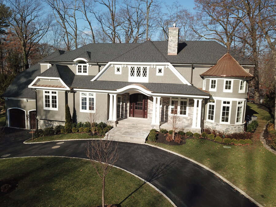 Gray shingle-style house with a dark roof and a round copper-roofed turret over a curved driveway