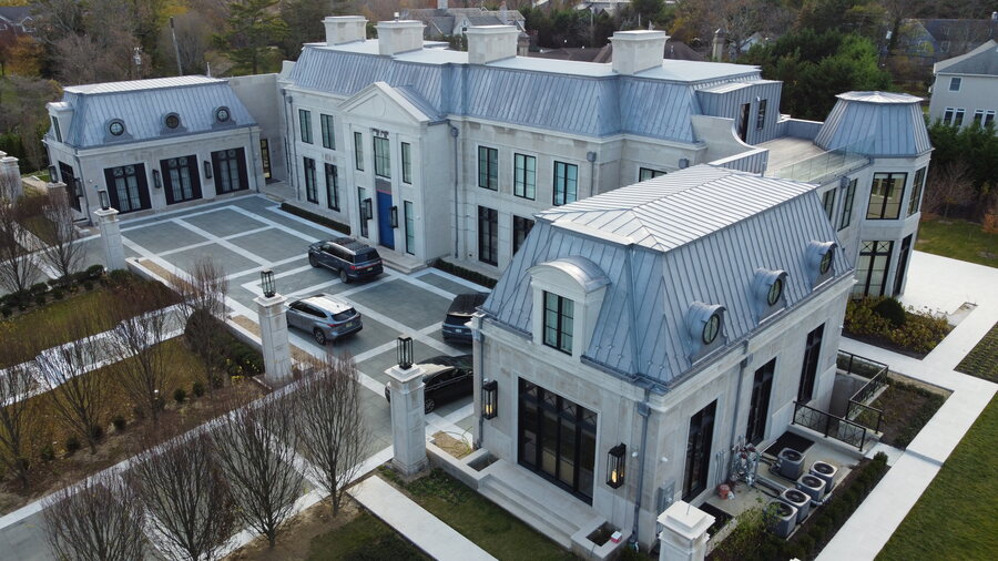 Aerial view of a limestone house with light gray standing-seam metal roofing and metal-clad dormers