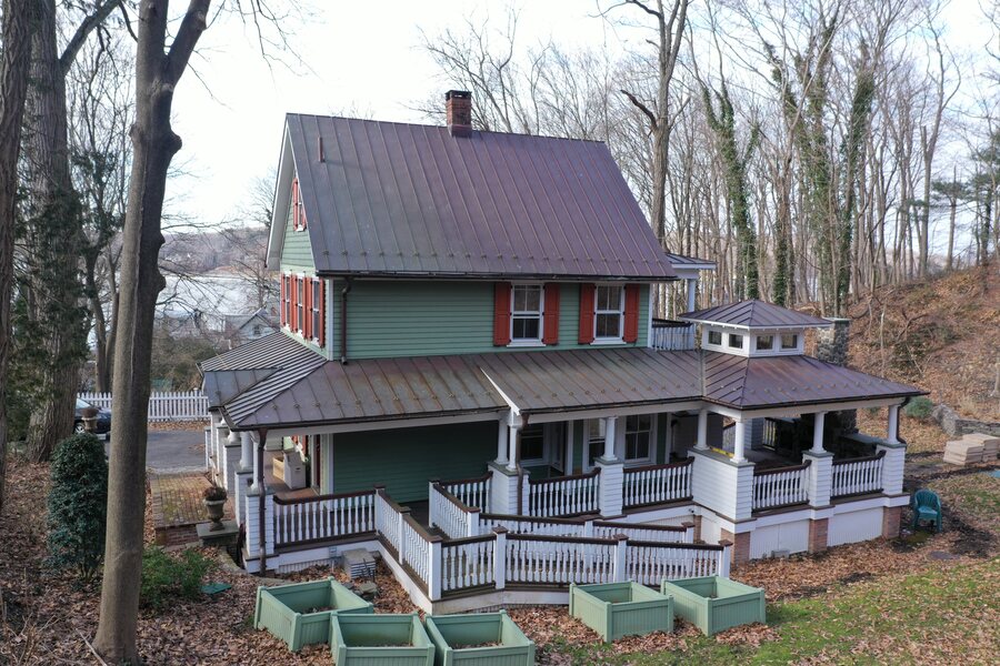 Craftsman-style house with a dark standing-seam metal roof and a wraparound porch with white railings