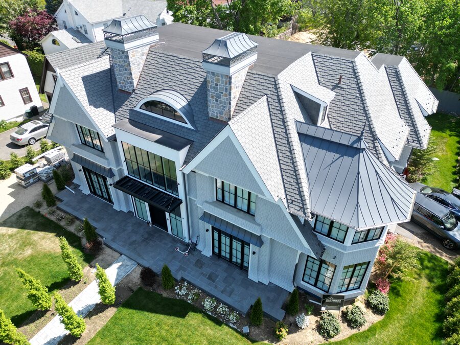 Aerial view of a gray house with a slate-look roof, standing-seam metal sections and a round turret
