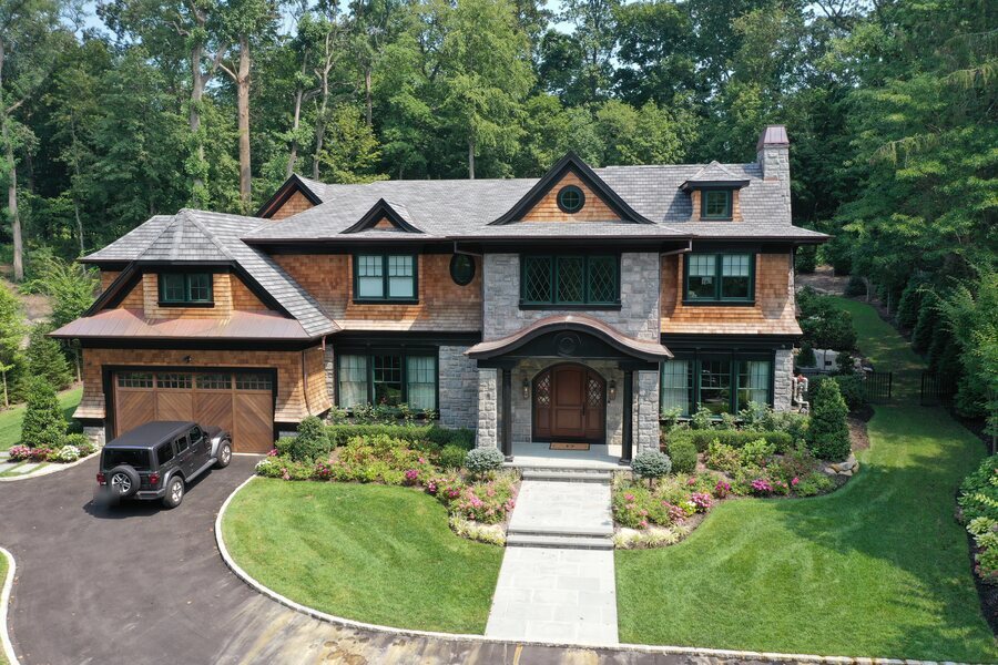 Stone and cedar-shingle house with a copper eyebrow roof over the entry and an arched wood door