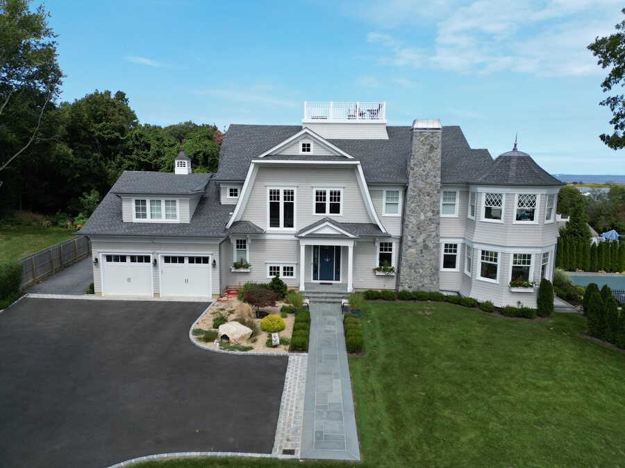 Gray shingle house with gambrel gables, a round tower bay and a tall stone chimney