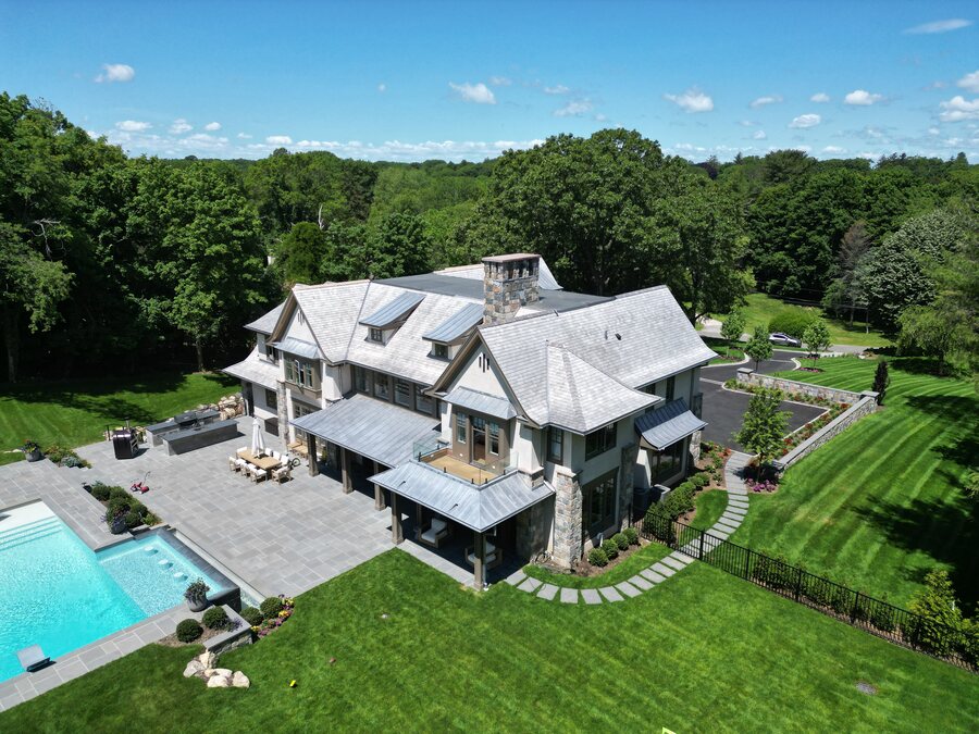 Aerial view of a gray house with a slate-look roof, metal awnings and a backyard pool