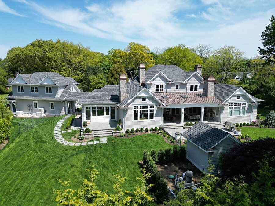 Gray house with a dark slate-look roof, a copper-colored porch roof and a lawn with stepping stones